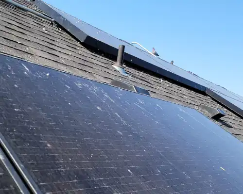 Solar panels on the roof of a house against a bright blue day sky.